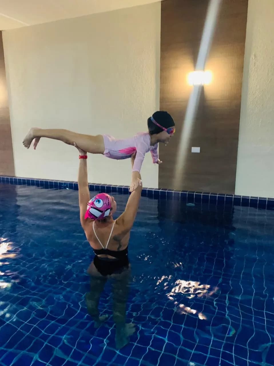 Professora na piscina coberta erguendo uma aluna em posição de voo