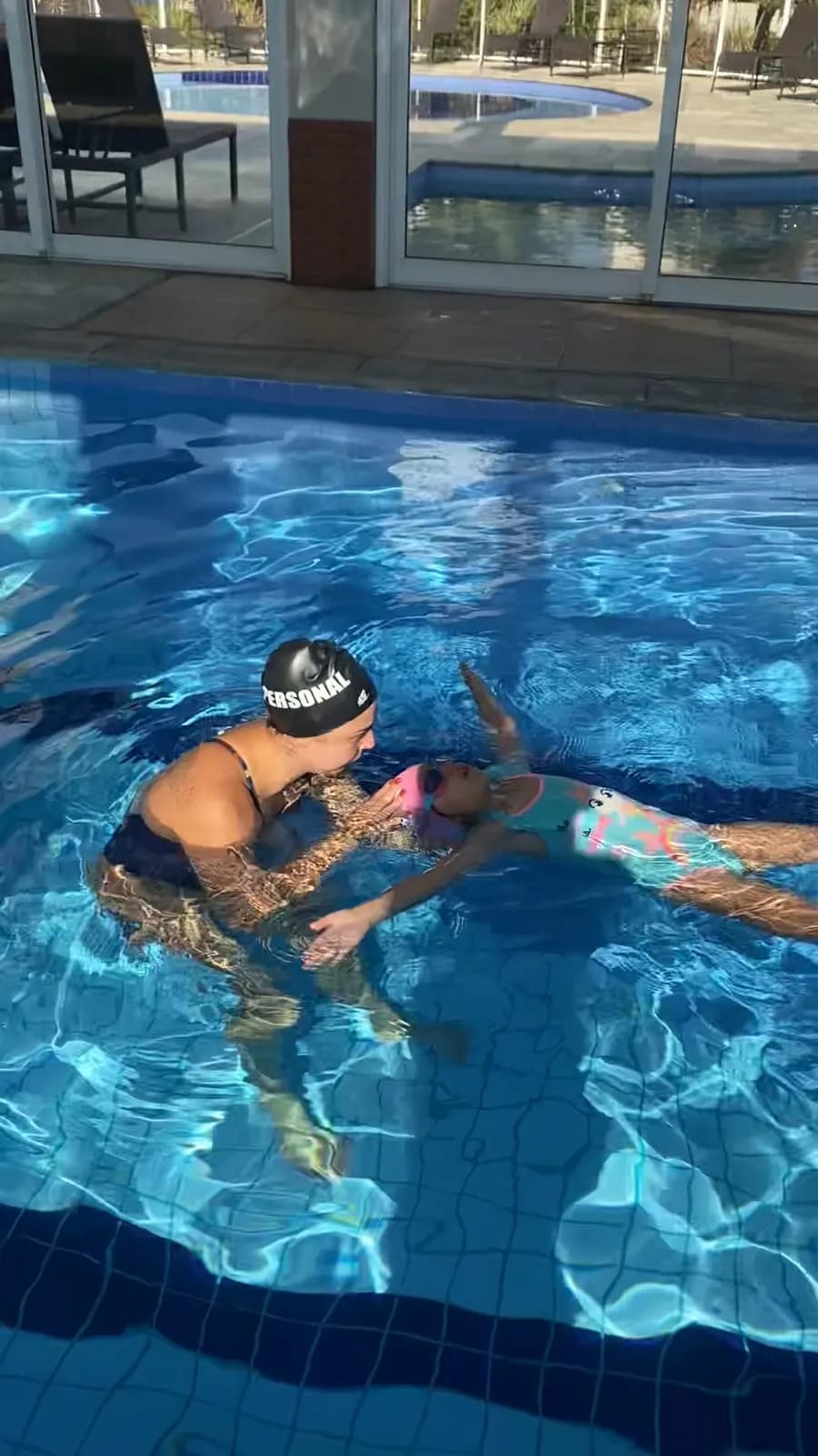 Professora dentro da água ensinando uma criança a flutuar