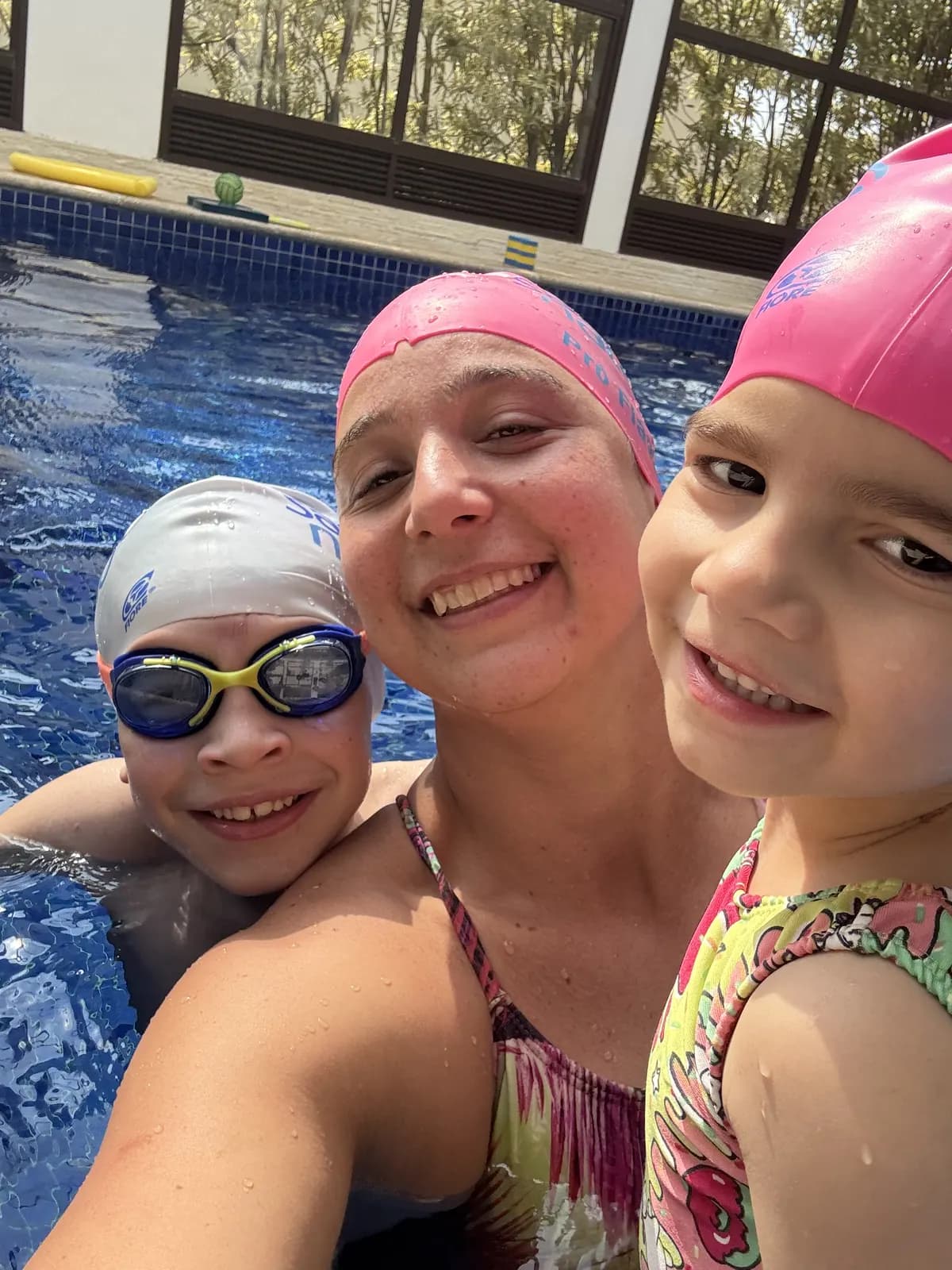 Mãe e dois filhos sorrindo juntos dentro da piscina