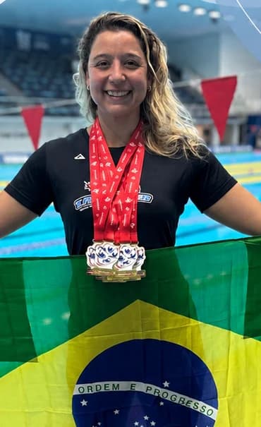 Flávia Turini, fundadora de Sampa Natação, con medallas y la bandera de Brasil en la piscina