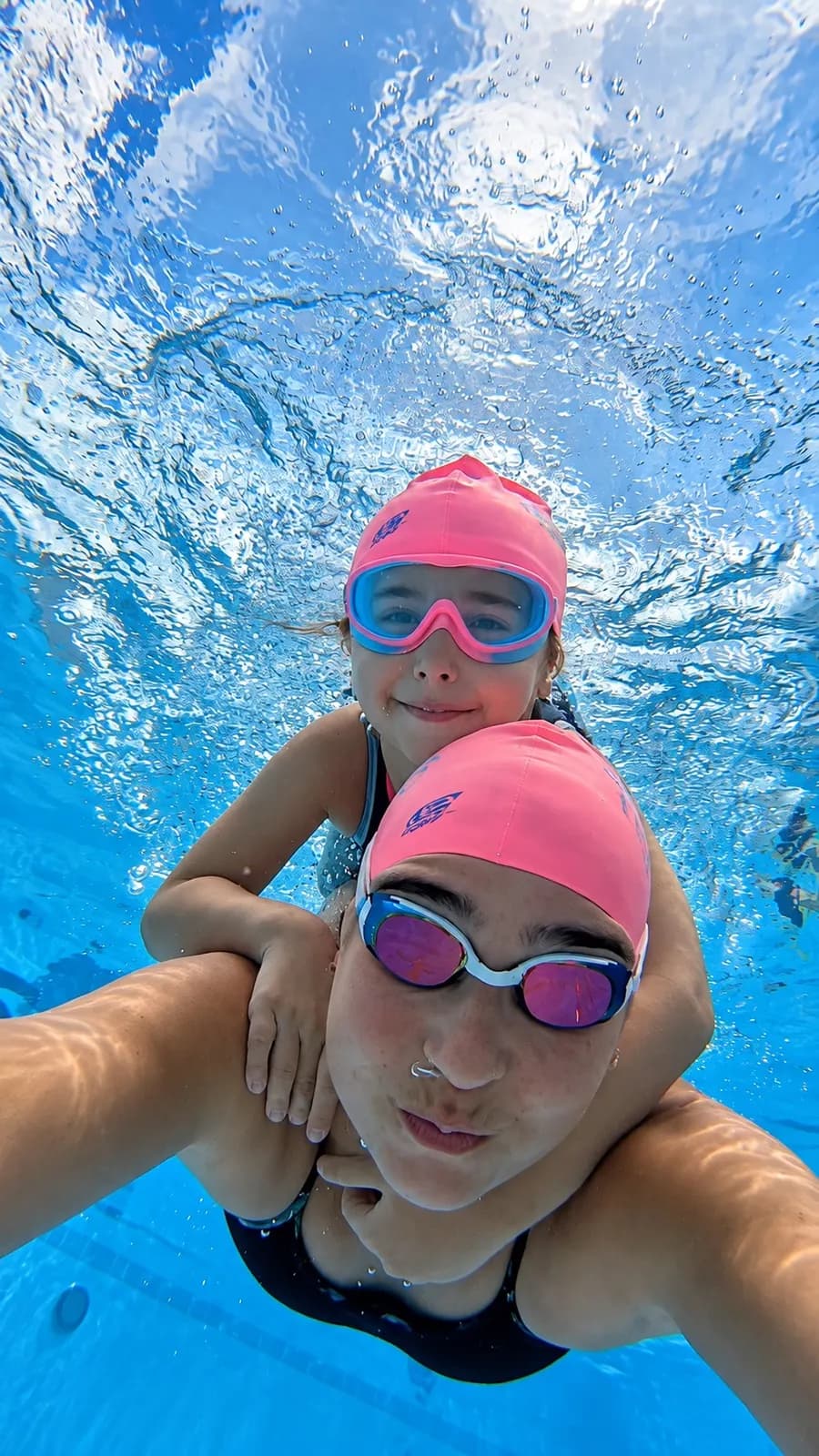 Mother and daughter in pink caps and goggles diving together, underwater photo