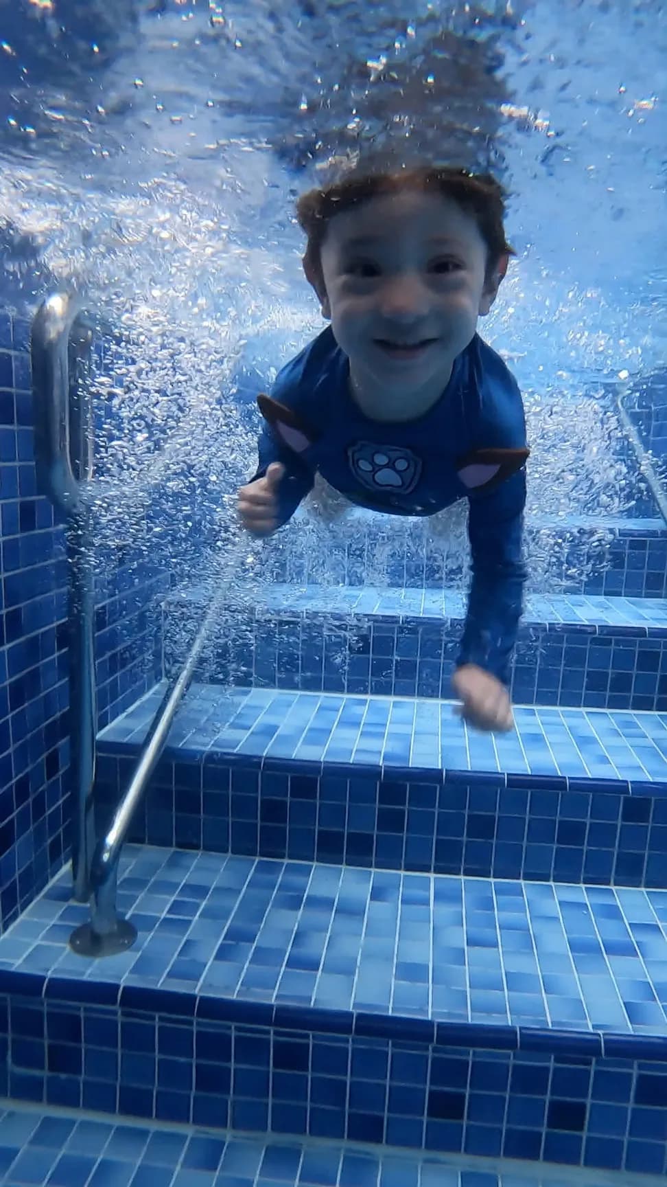 Boy smiling underwater giving a thumbs up on the pool ladder
